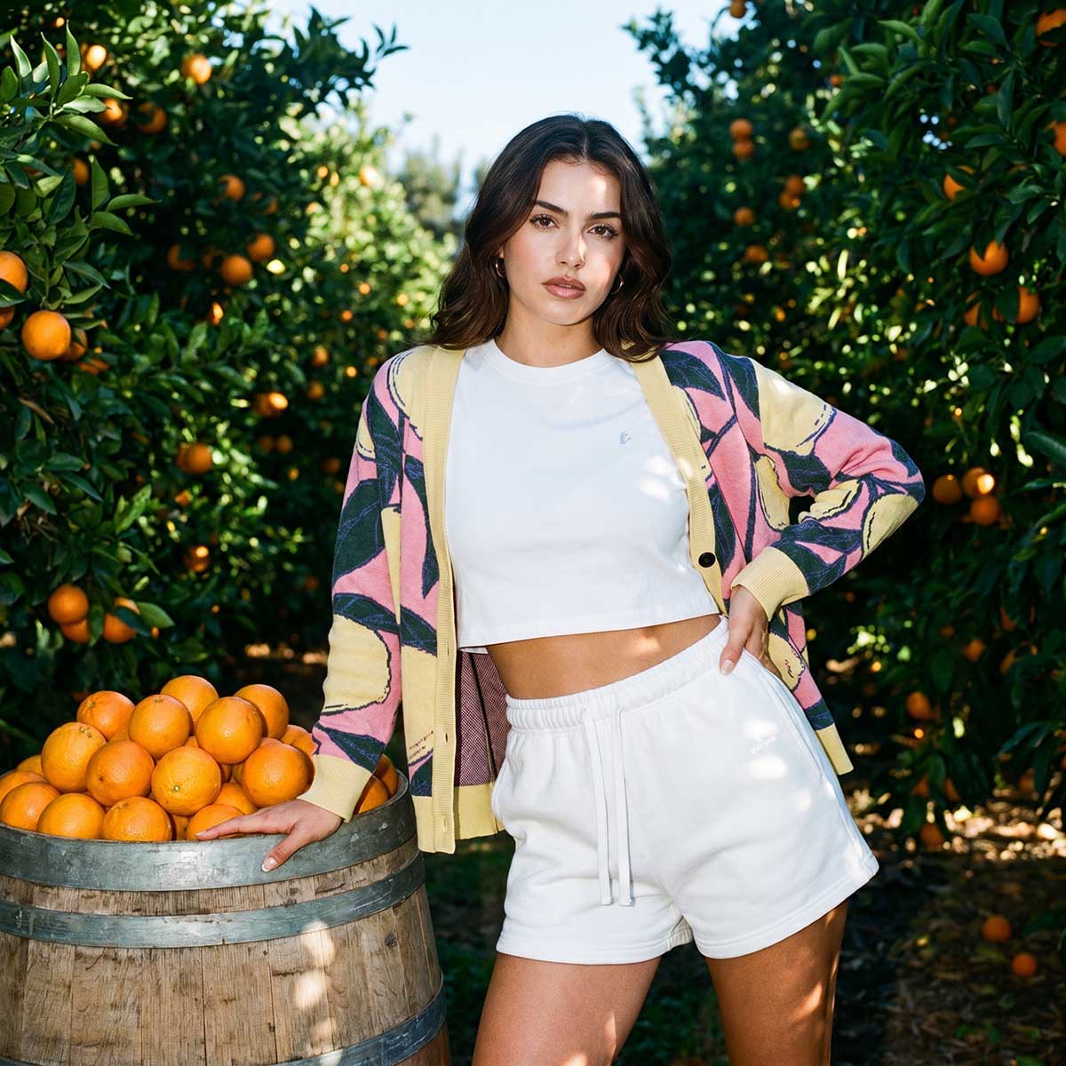 Woman standing next to a barrel of oranges in an orange grove