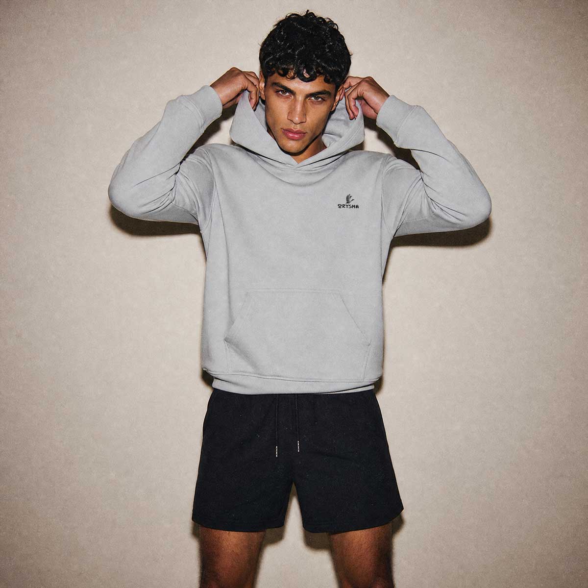 Person wearing a gray hoodie with a brand logo on a beige background