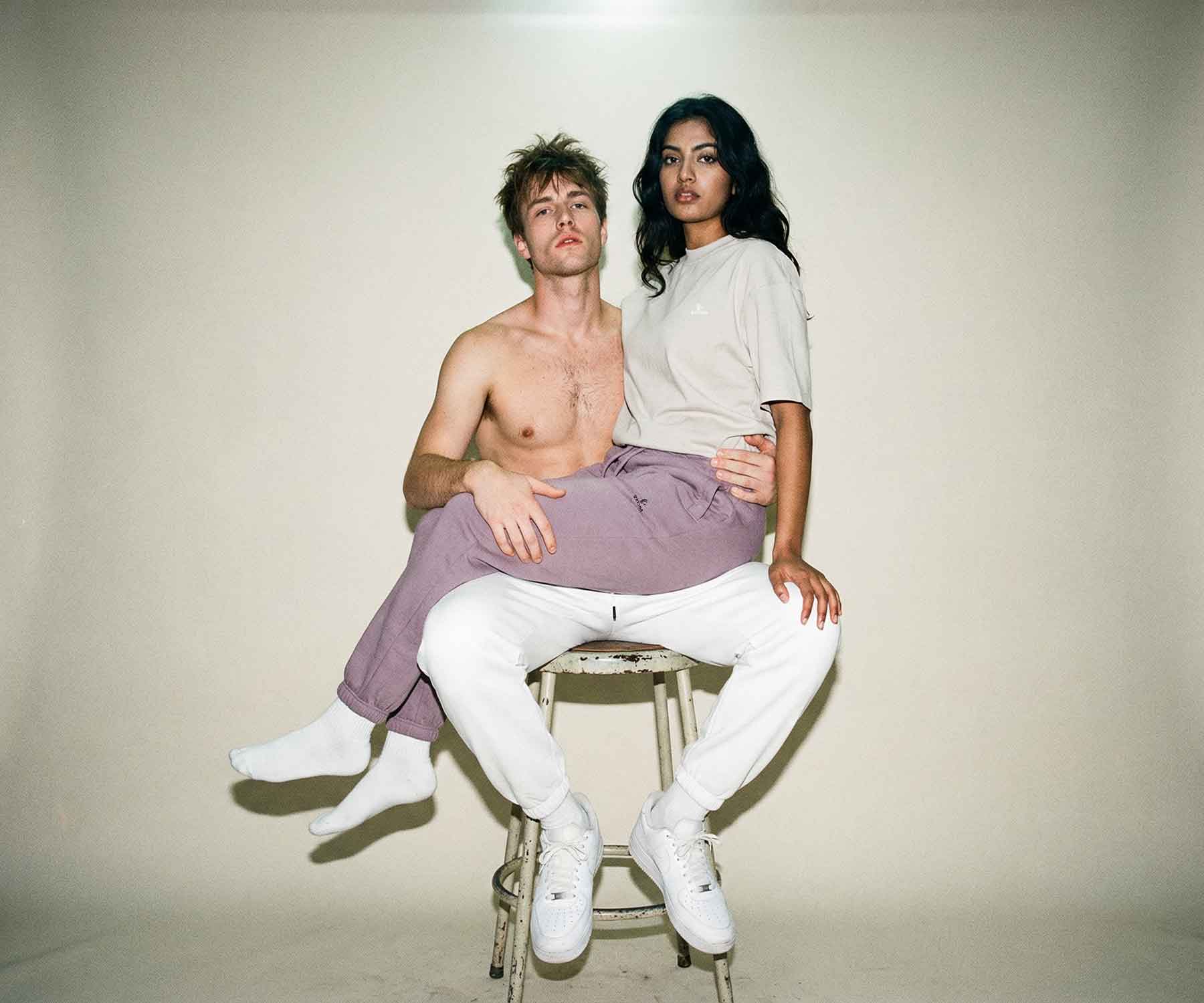 Two people sitting on a stool against a plain background