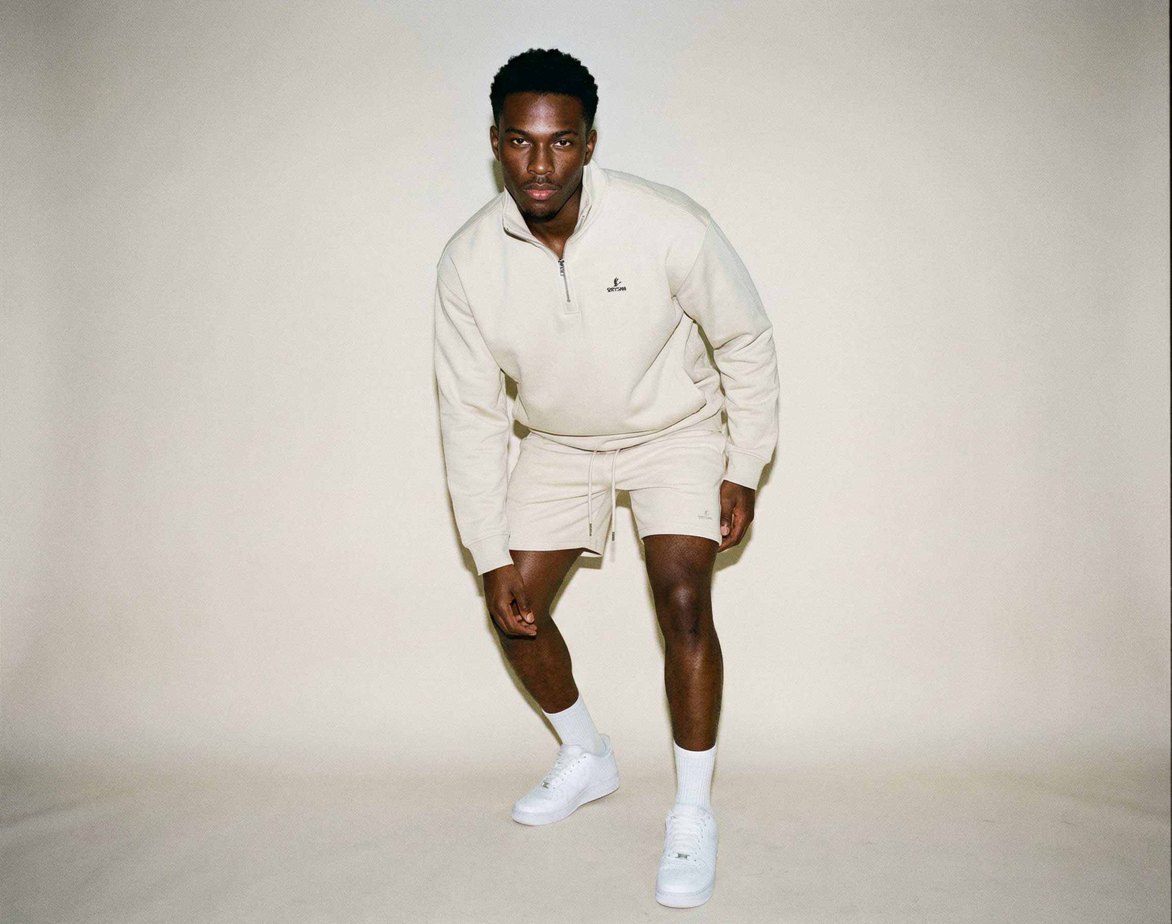 Man wearing a cream-colored outfit with a logo on a plain background