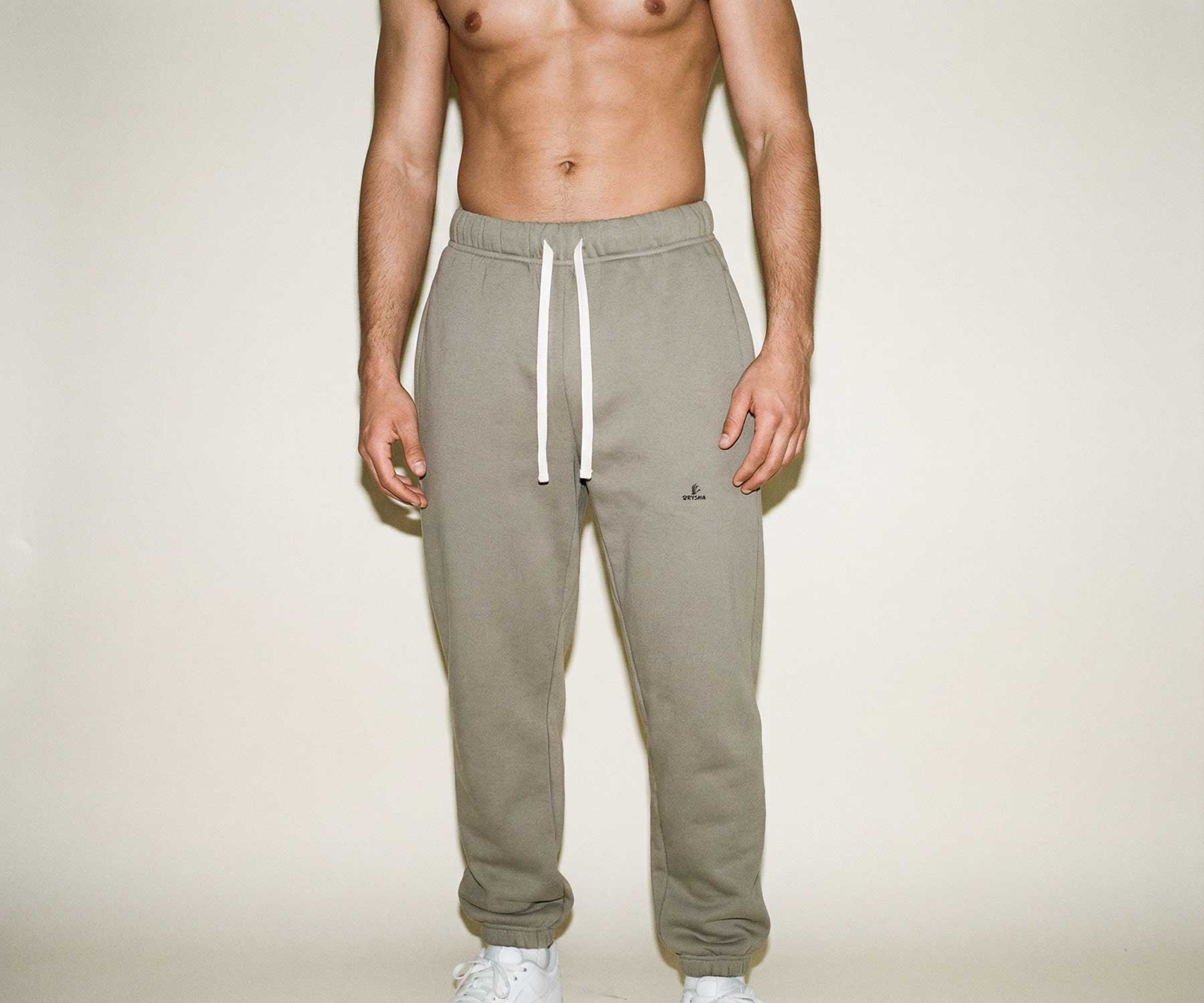 Person wearing beige sweatpants with a logo on a plain background