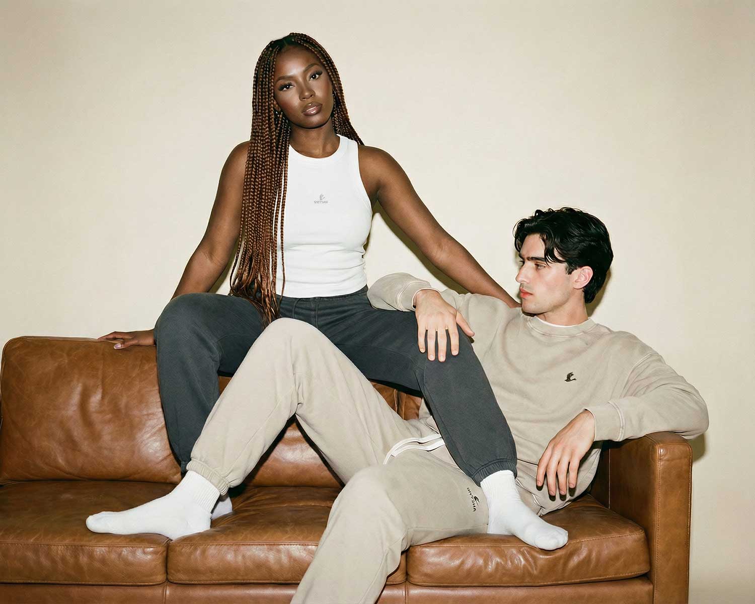 Two people sitting on a brown leather couch against a plain background