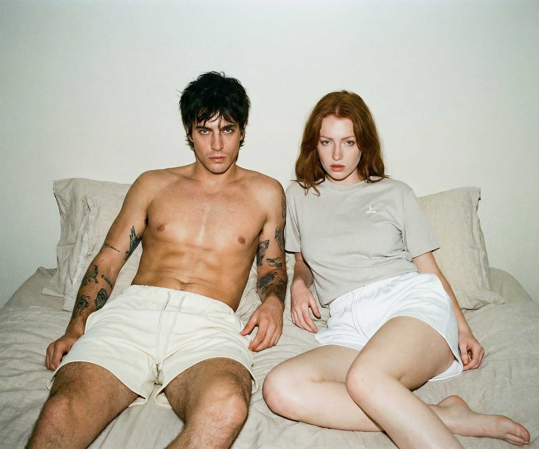 Two people sitting on a bed wearing matching white shorts.