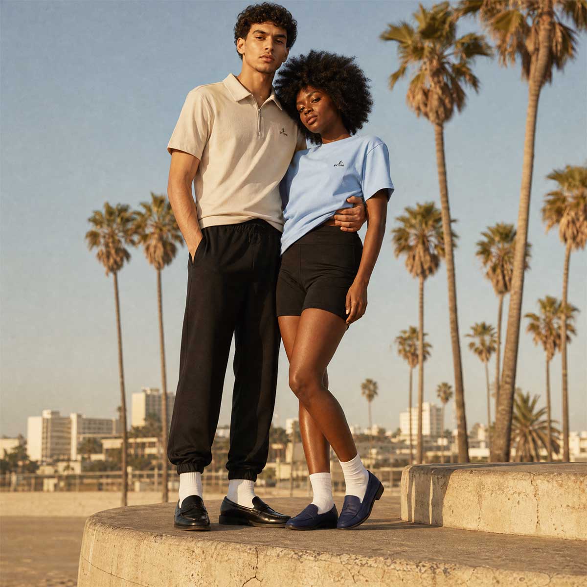 Two people standing together with palm trees and a city skyline in the background