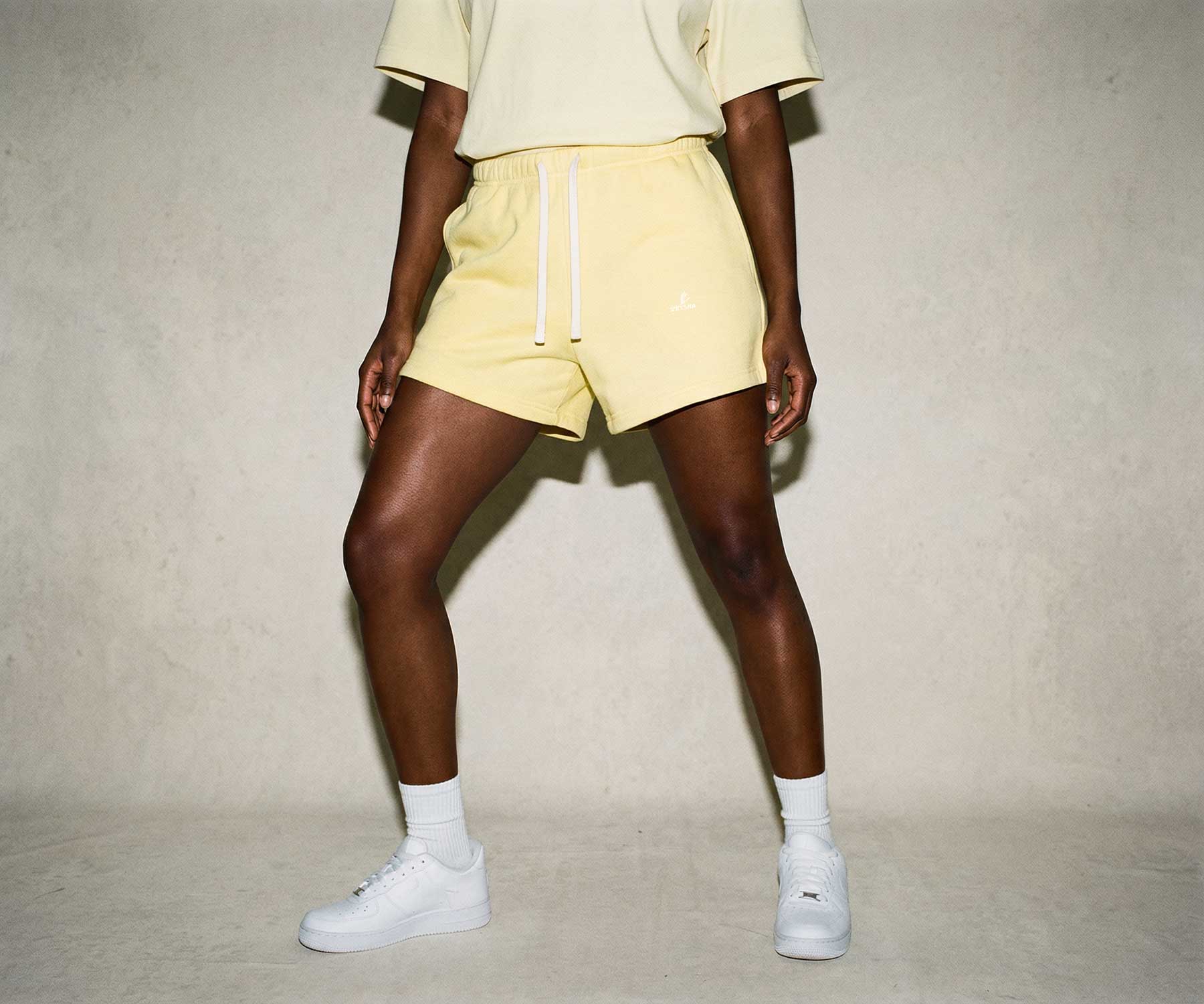 Person wearing a light yellow outfit with shorts and a shirt, standing against a plain background.