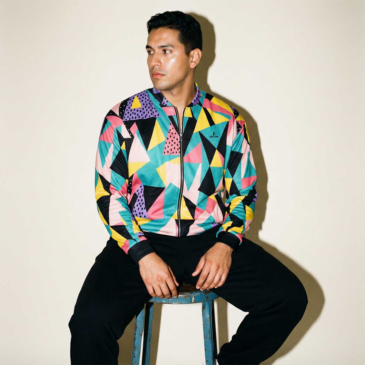 Man wearing Orysha men’s colorful geometric print track jacket with zip-up front, styled with black pants in a modern studio streetwear look