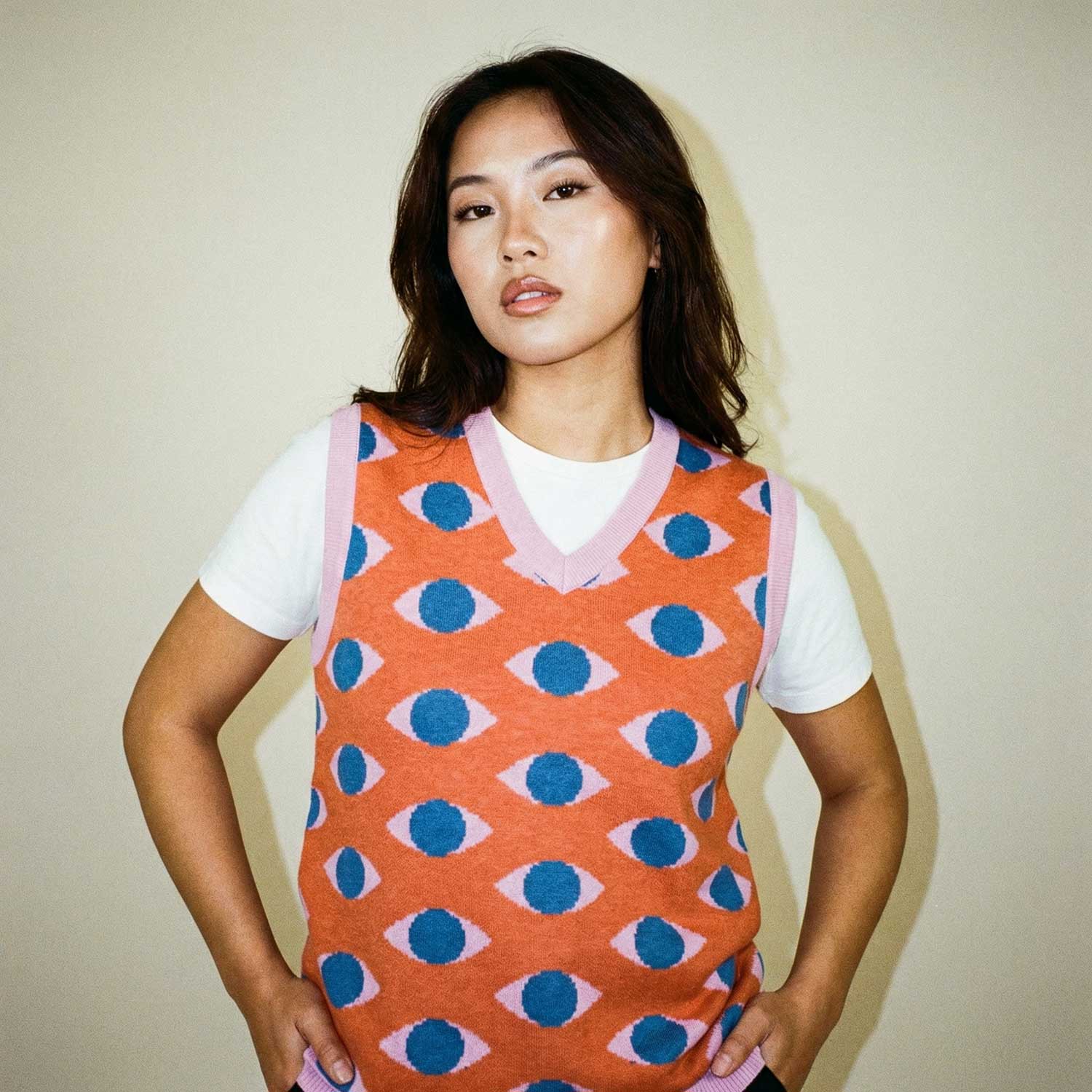Woman wearing Orysha women’s orange knit vest with eye pattern design layered over a white t-shirt, modern artistic streetwear look