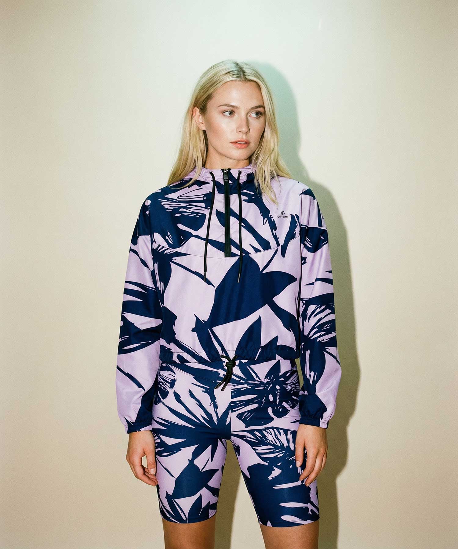 Woman wearing Orysha women’s purple tropical print windbreaker jacket with matching biker shorts, styled in a modern studio streetwear look