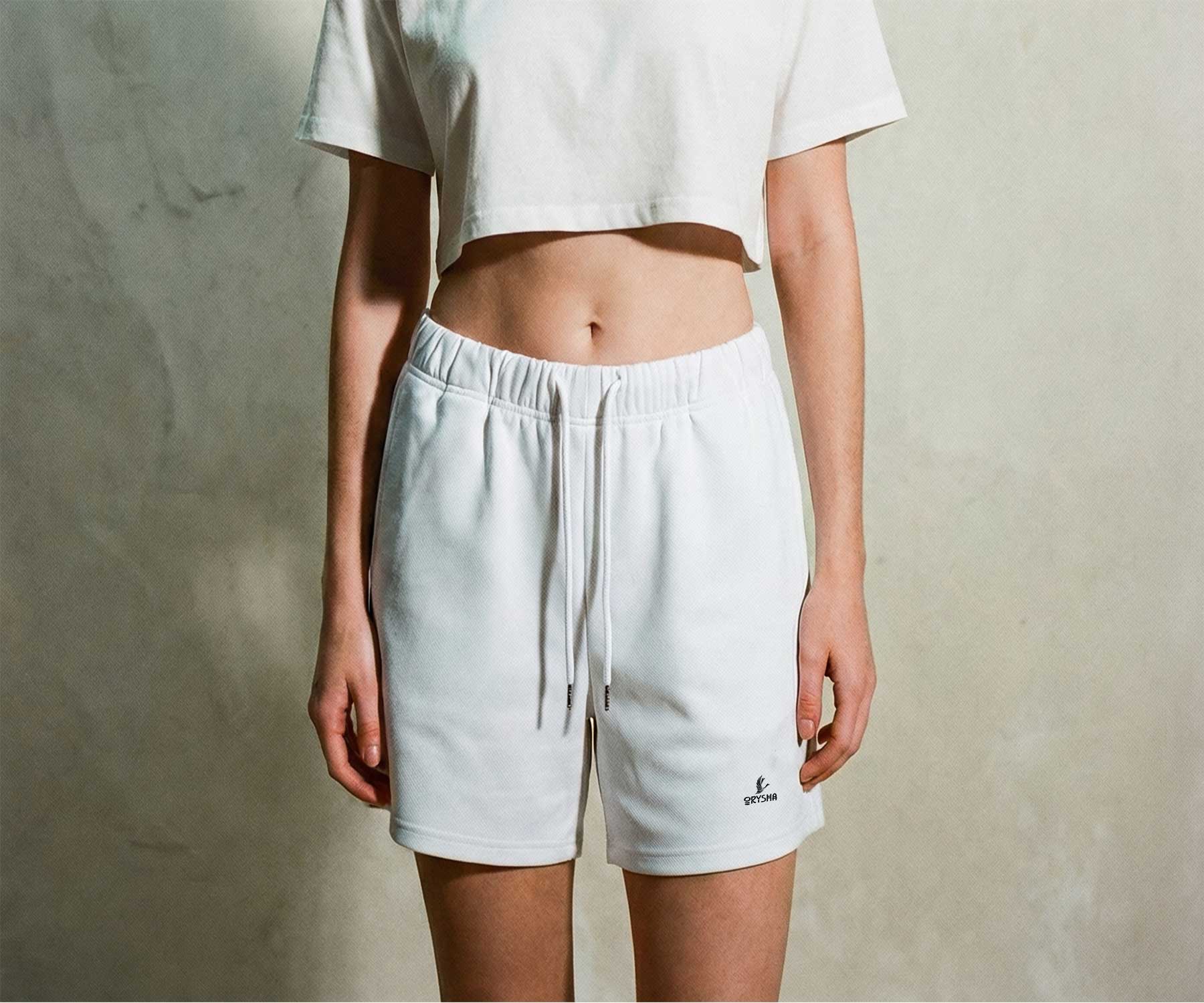 Woman wearing Orysha women’s white athleisure shorts with drawstring waist and embroidered logo, styled with a cropped white top in a minimalist fashion editorial