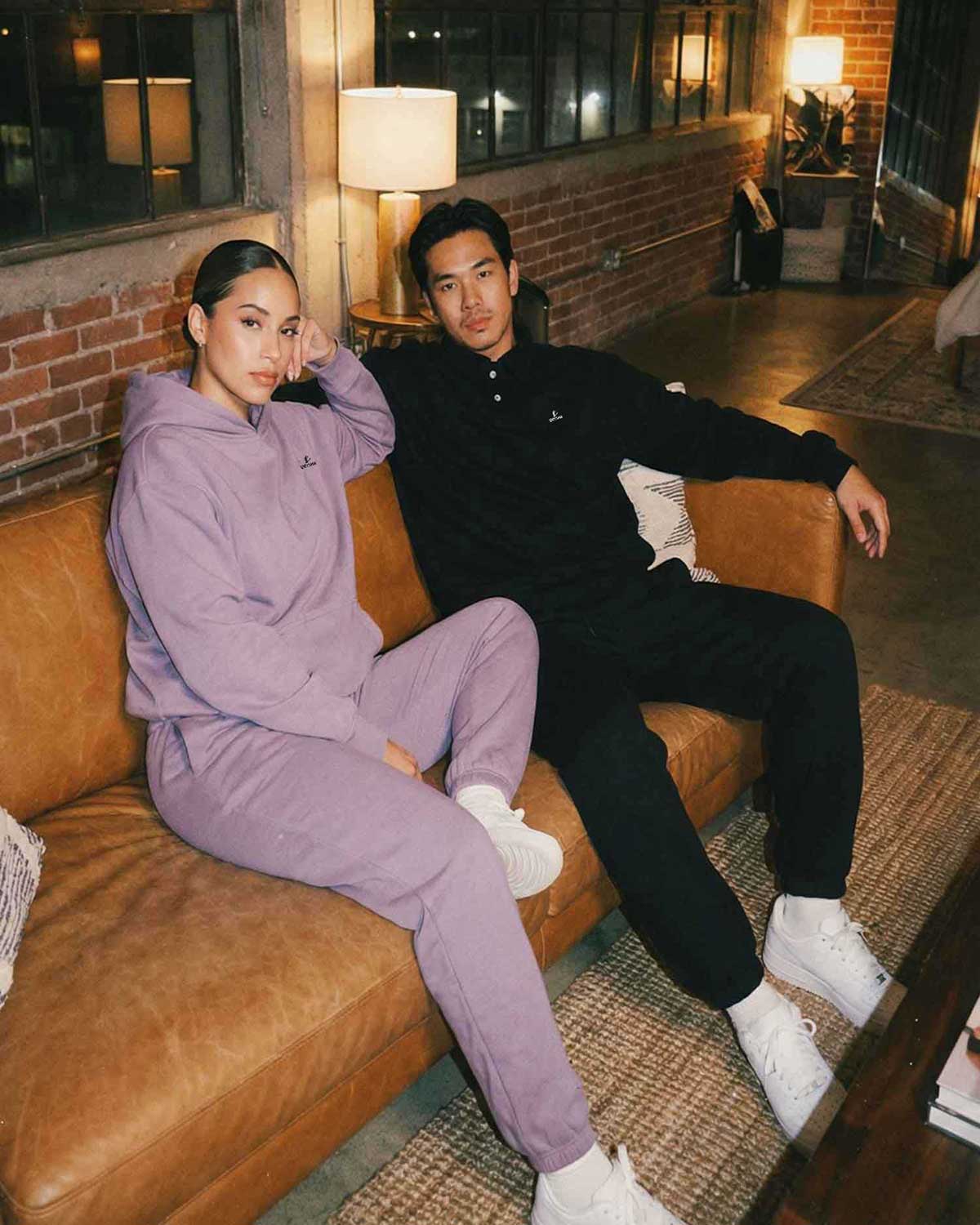 Two people sitting on a brown couch in a cozy room with brick walls and lamps.
