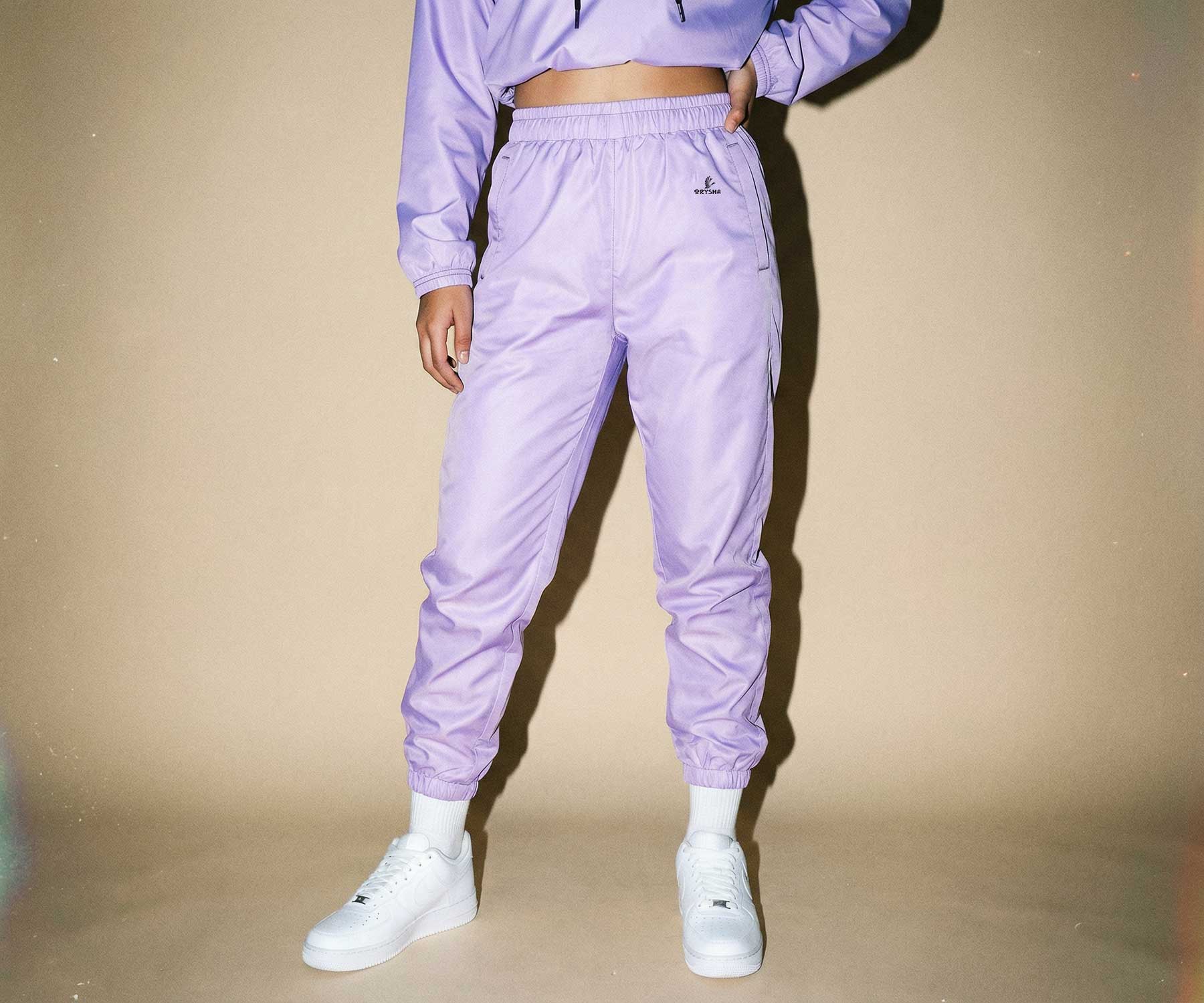 Person wearing a matching lavender tracksuit with white sneakers on a beige background